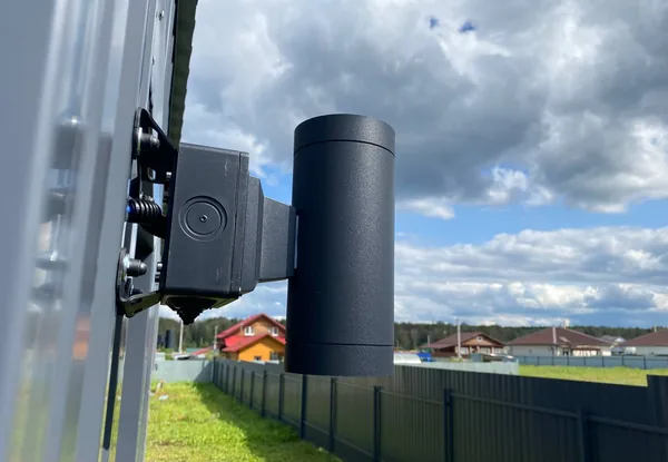 Крупный план коробки BOXFORCAM™ на столбе ограждения, за забором видны дома посёлка
