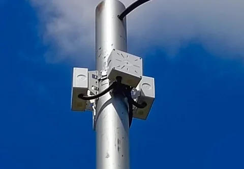 Три коробки BOXFORCAM™ закреплены вокруг металлической опоры освещения, фон — синее небо